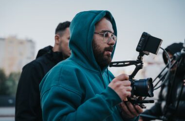 Shooter cradling small mirrorless in cage with top monitor, on location