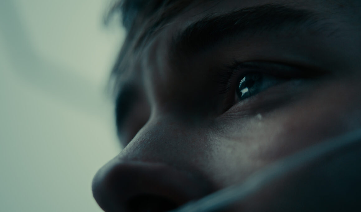 Cinematic extreme close-up of a young man's eye with a tear on his cheek in a cool, desaturated grade