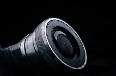 Close-up of a silver mirrorless camera lens angled against a black background, with reflections on the glass and barrel