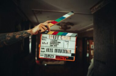 A hand holding a colour-chip film slate marked 25FPS in a dark interior hallway