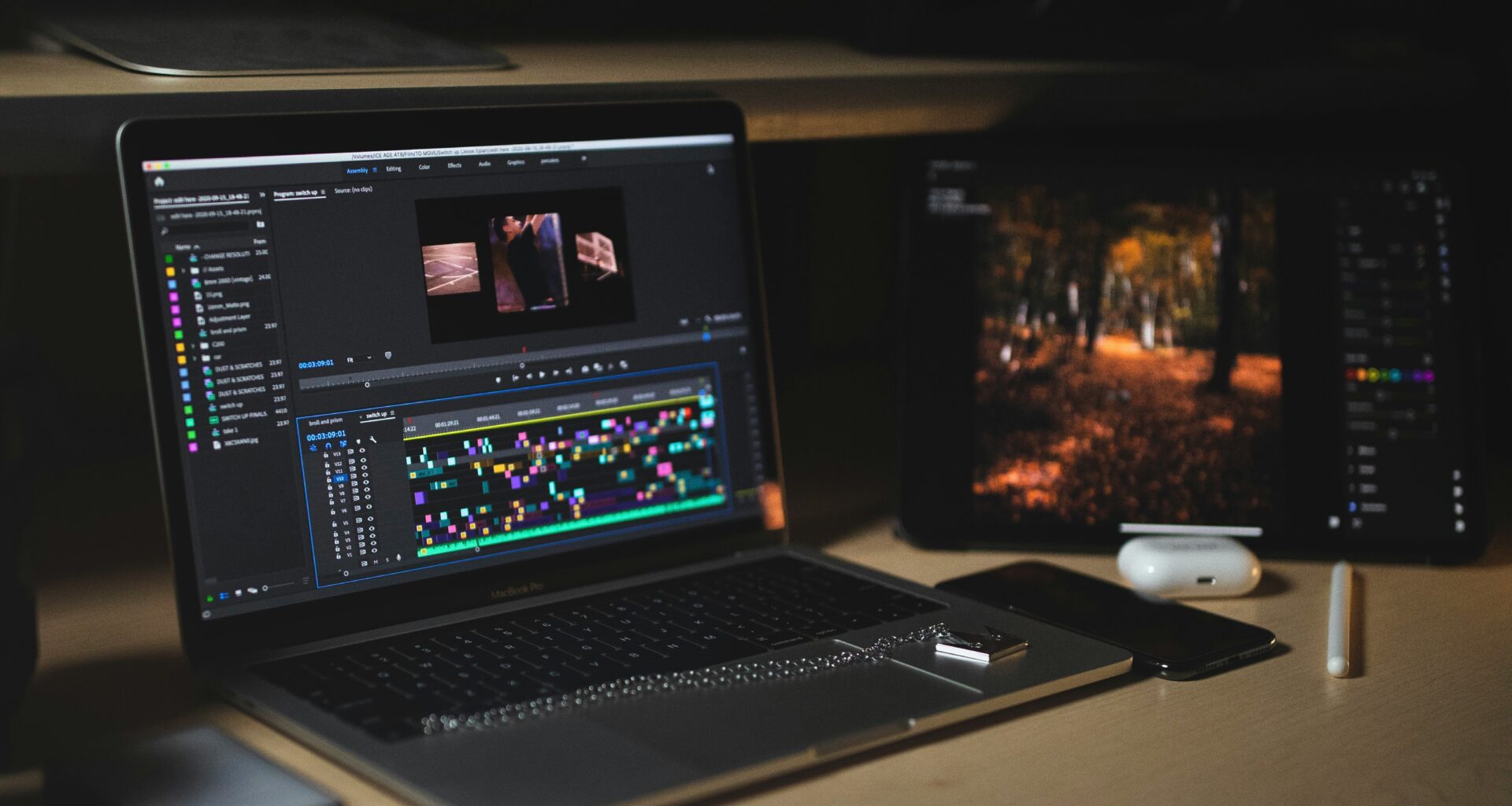 MacBook Pro with a Premiere Pro timeline open on a desk in a dark edit space
