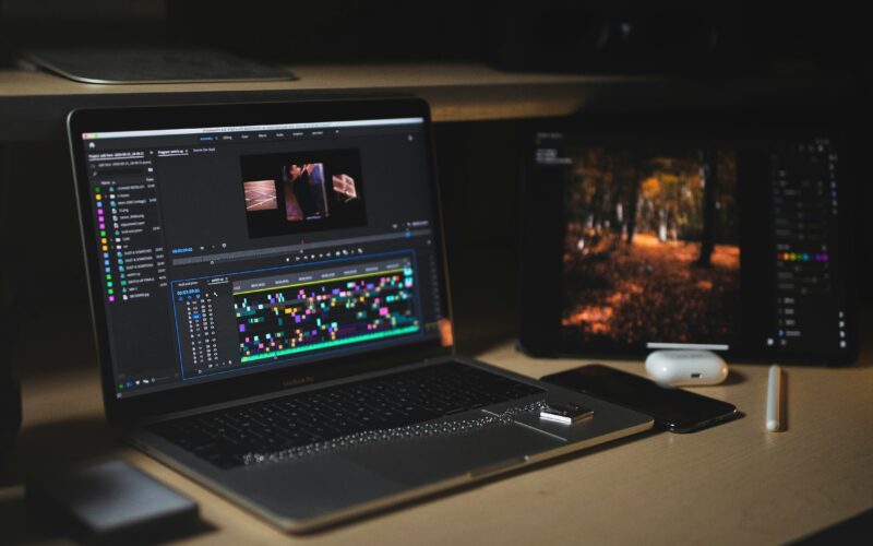 MacBook Pro with a Premiere Pro timeline open on a desk in a dark edit space