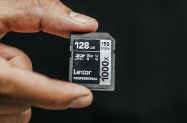 A hand holding a Lexar 128GB SD card against a dark background