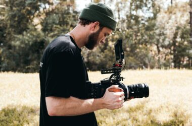 Bearded videographer filming outdoors in field with professional camera gear