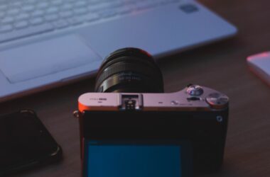 A mirrorless video camera on a wooden desk beside a laptop