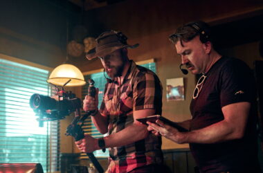Camera operator shooting with a Sony FX5 on a gimbal in a dimly lit diner set while a director checks a tablet