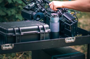 Hand on camera atop road cases, V-mount batteries, wireless TX