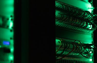 A rack of network servers and tangled patch cables glowing green in a dark server room