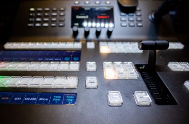 Close-up of a darkened video production control surface with rows of illuminated buttons and a T-bar fader