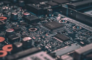 Macro photograph of a dark teal circuit board with a processor chip in focus, surrounded by capacitors and solder points
