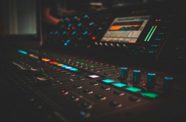 Close-up of a lit digital audio mixing console in a dark studio, with an orange waveform on its small screen