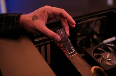 A hand holding a Samsung 990 Pro M.2 NVMe SSD above the motherboard of an open desktop PC