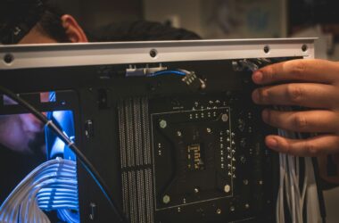 Hands working inside an open PC case in low light, with the bare CPU socket, memory slots and blue sleeved cables visible