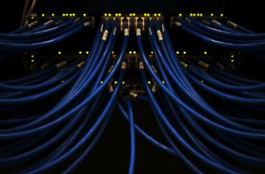 Blue network patch cables fanning out from a lit switch panel in a dark server rack