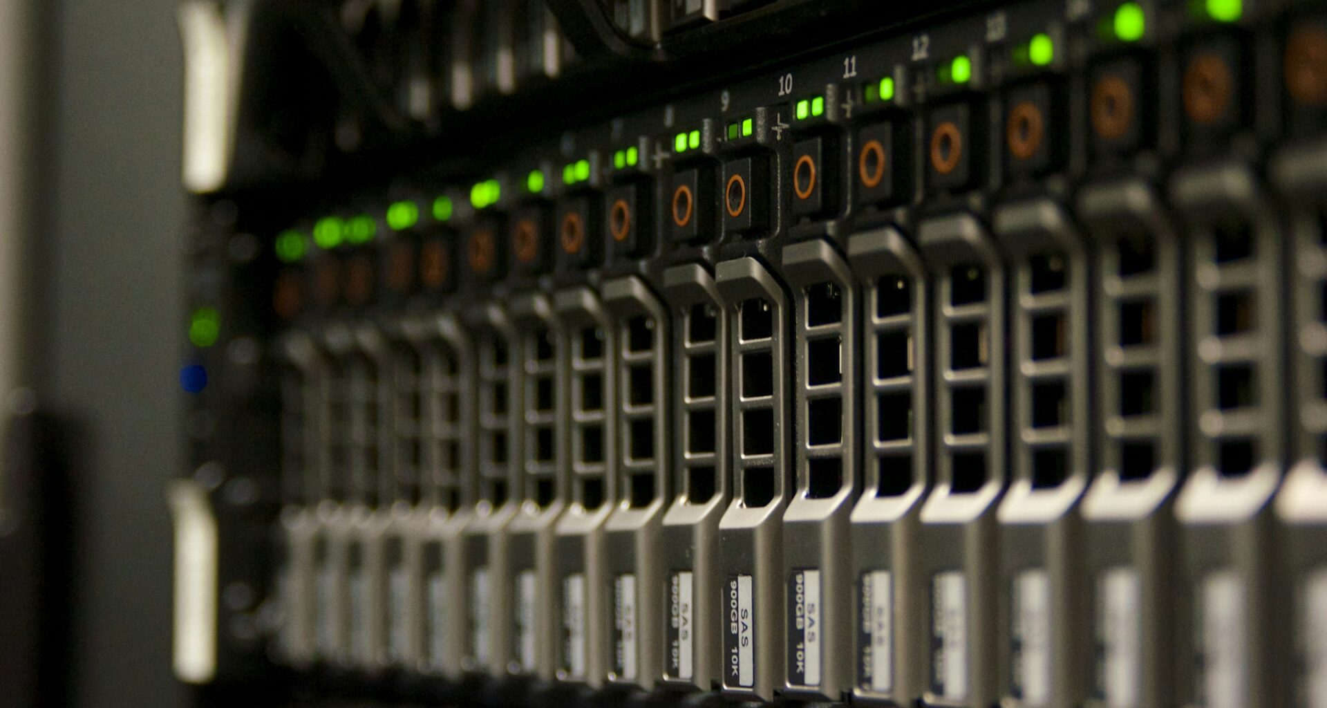 Rows of hard drive caddies in a multi-bay storage array, green status LEDs lit in a dark room