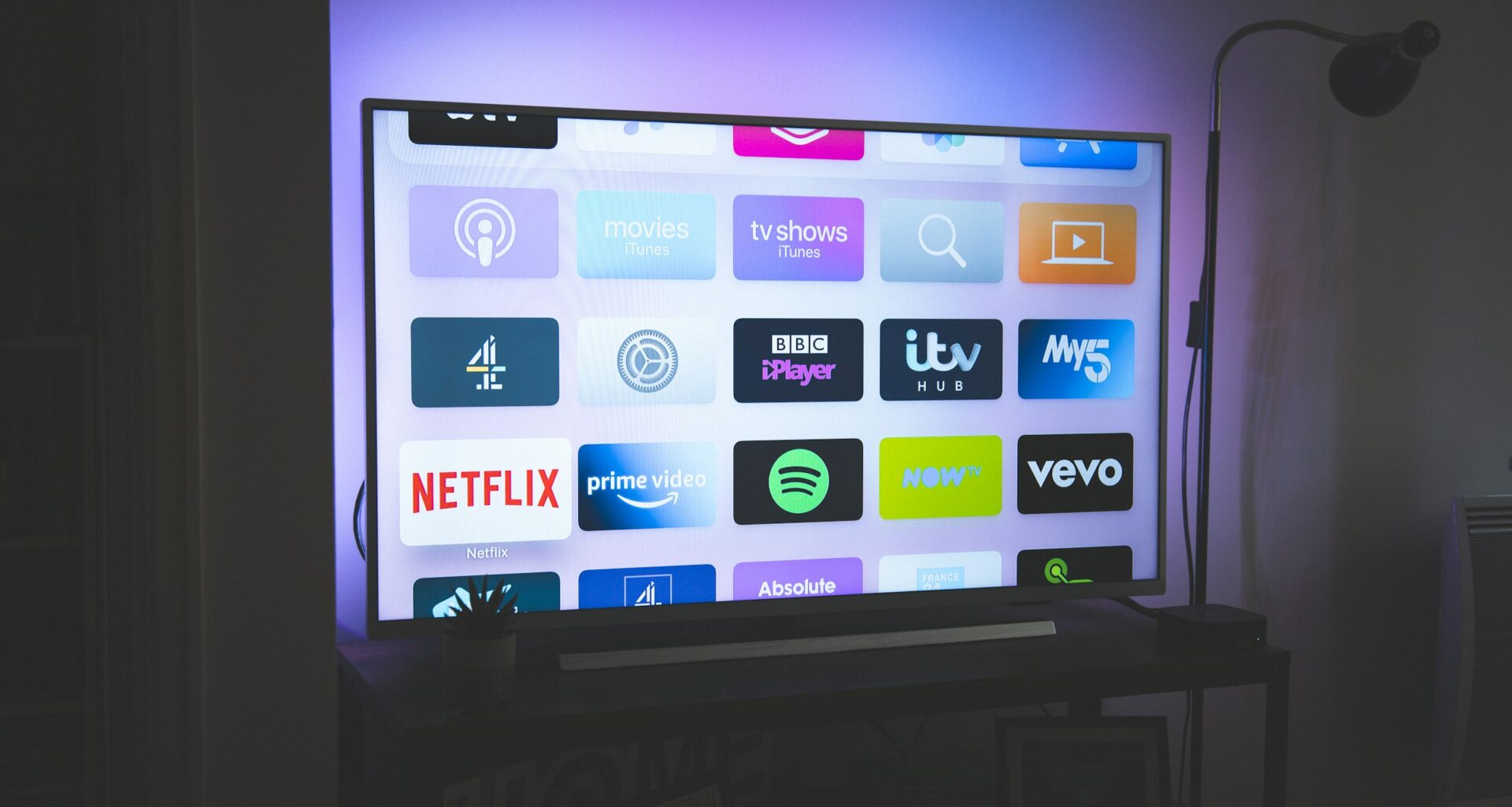 A large flat-screen TV glowing in a dark room with coloured bias lighting behind the panel