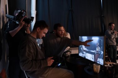 A man gestures toward a video playback monitor while a colleague watches in a dark studio