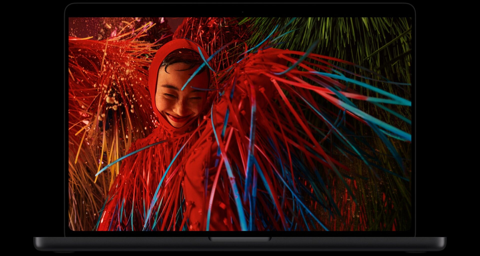 A space black MacBook Pro with PROLED XDR Display showing a red-lit portrait with neon streaks on screen