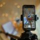 A phone mounted on a small tripod recording a flat-lay scene with warm bokeh lights behind it