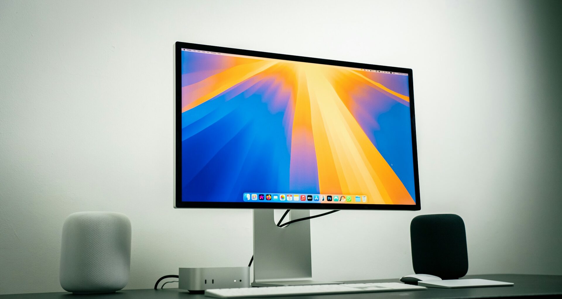 A 27-inch monitor on a desk with a Mac mini, keyboard and speakers