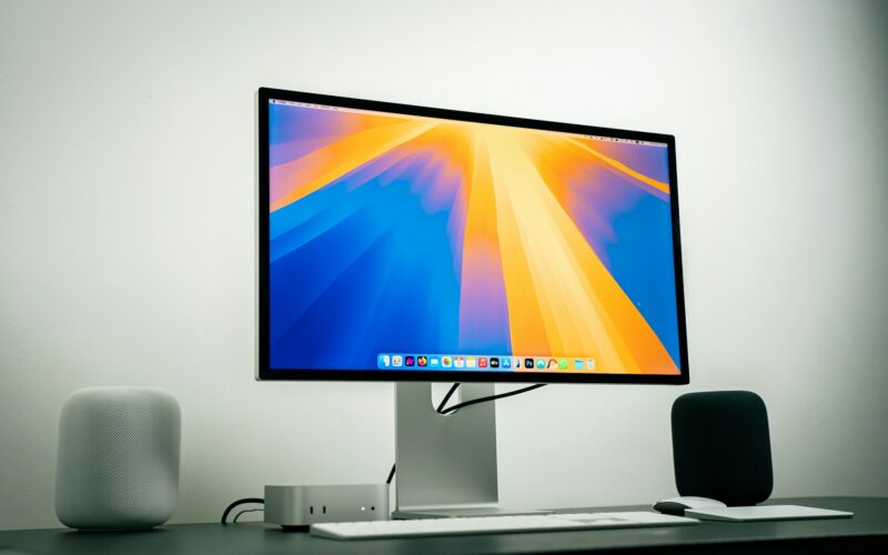 A 27-inch monitor on a desk with a Mac mini, keyboard and speakers