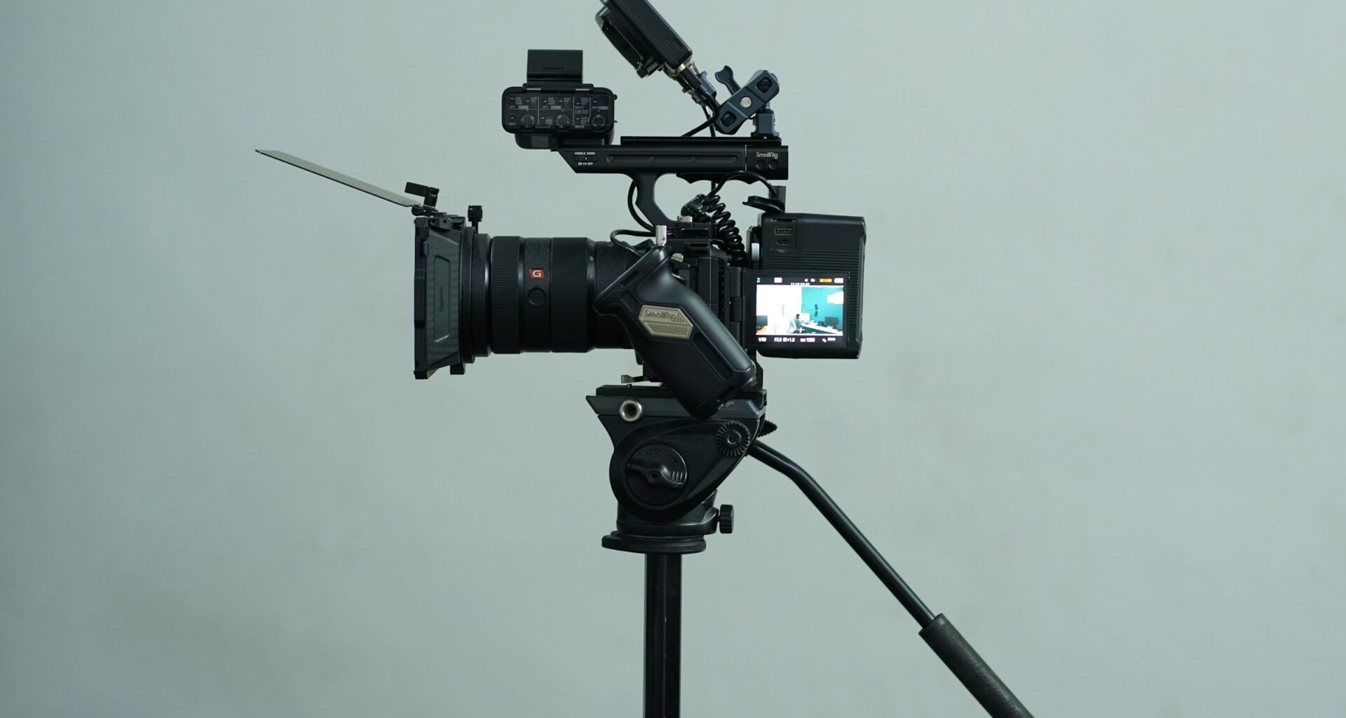 A Sony cinema camera rig on a fluid-head video tripod against a grey wall