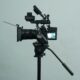 A Sony cinema camera rig on a fluid-head video tripod against a grey wall