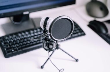 A USB microphone with a pop filter on a desk in front of a keyboard and monitor