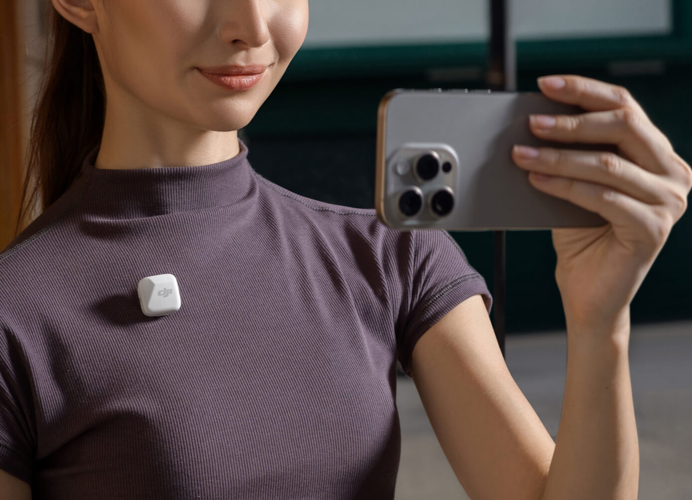 A creator filming herself with an iPhone, a white DJI Mic Mini transmitter clipped to her shirt