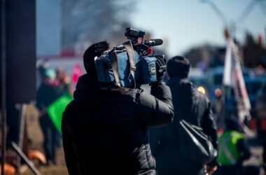 A news camera operator with a shoulder-mounted ENG camera filming at an outdoor event