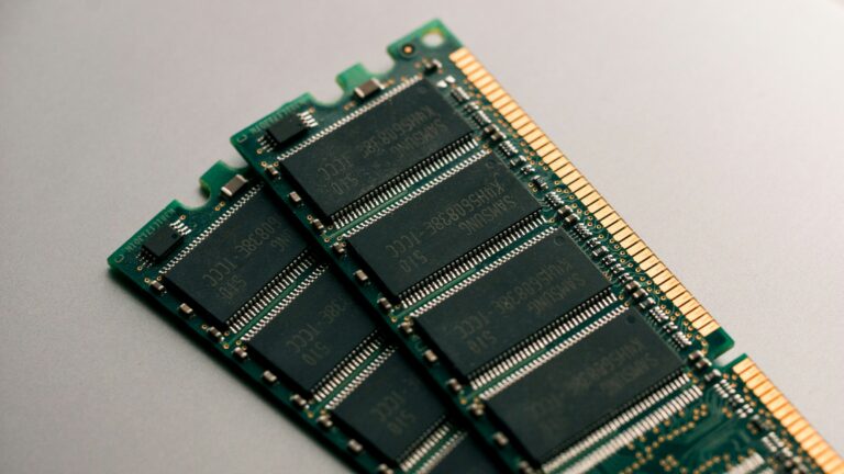 A DDR SODIMM memory module lying on a dark desk, chips and gold contacts in focus