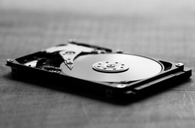 An opened 3.5-inch hard drive lying on a table, platter and read head exposed, in black and white